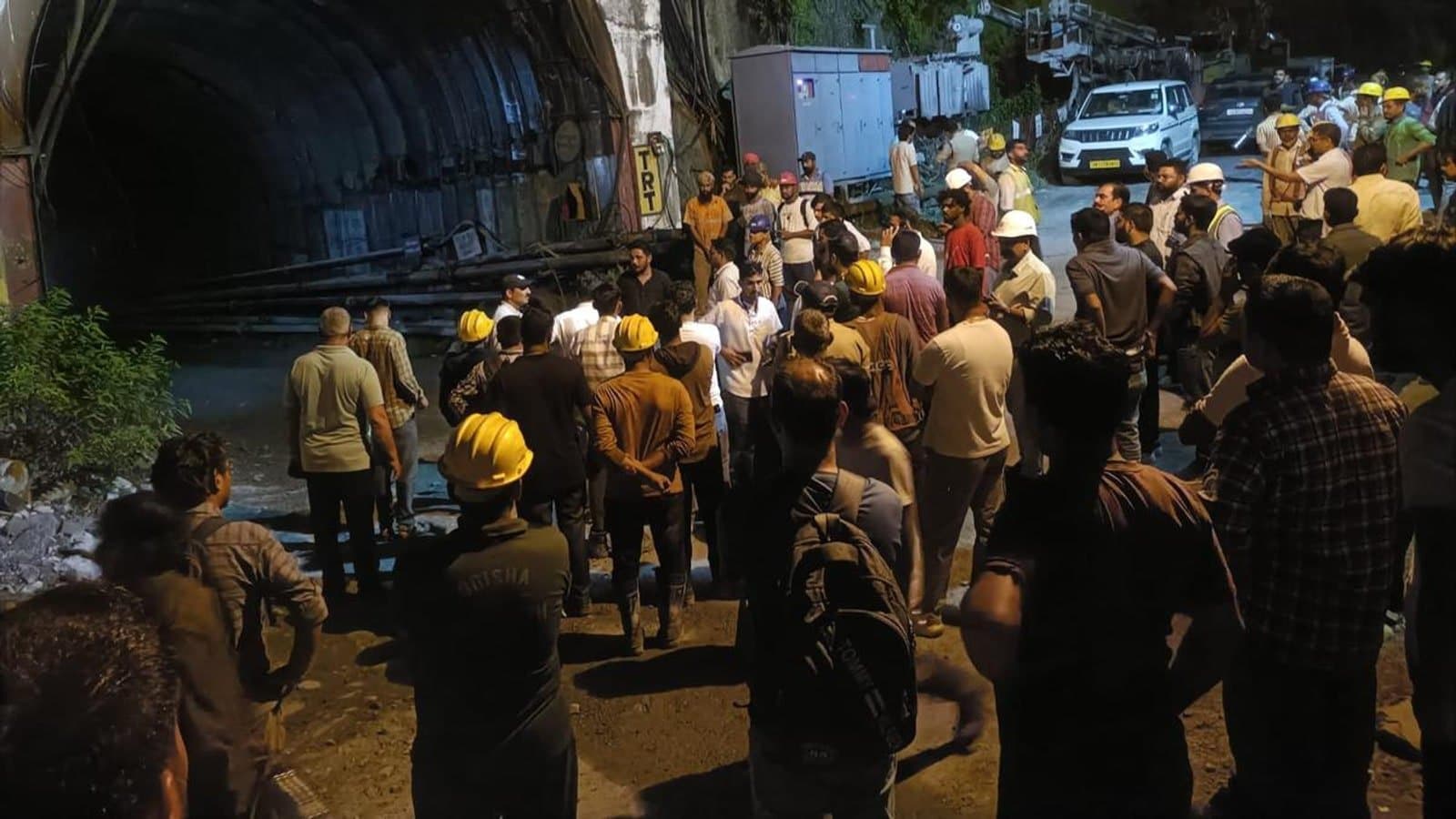 Rescue workers, police and officials in hard hats gathered at night outside the mouth of an under construction tunnel.