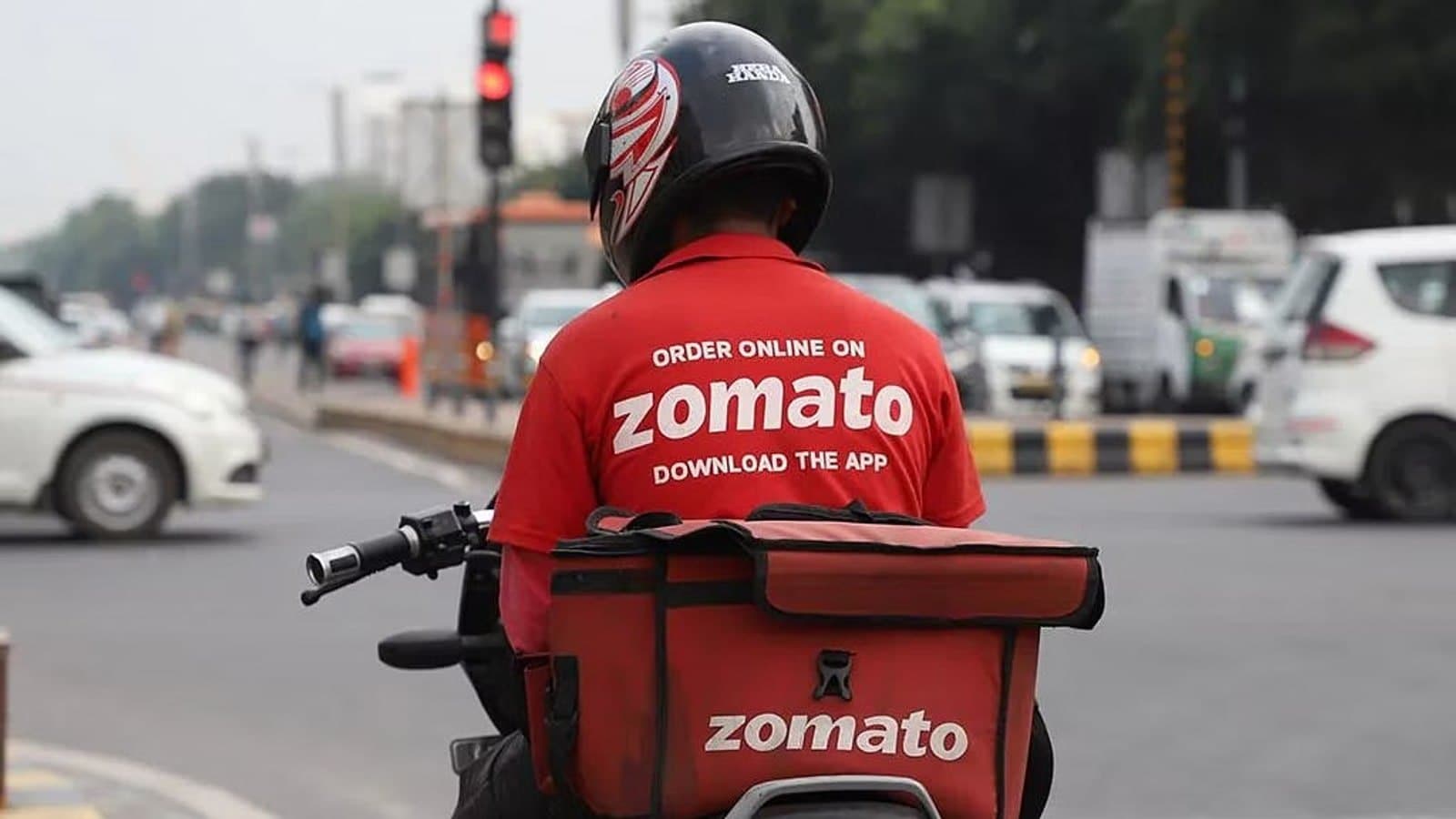 A Zomato delivery rider on a motorcycle at a traffic signal, seen from behind with an insulated delivery bag. फाइल फोटो।