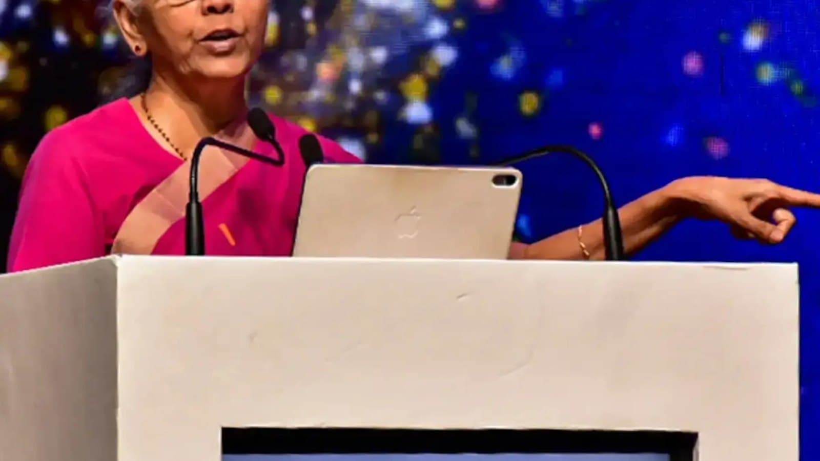Finance Minister Nirmala Sitharaman speaking from a lectern, gesturing while addressing an audience.