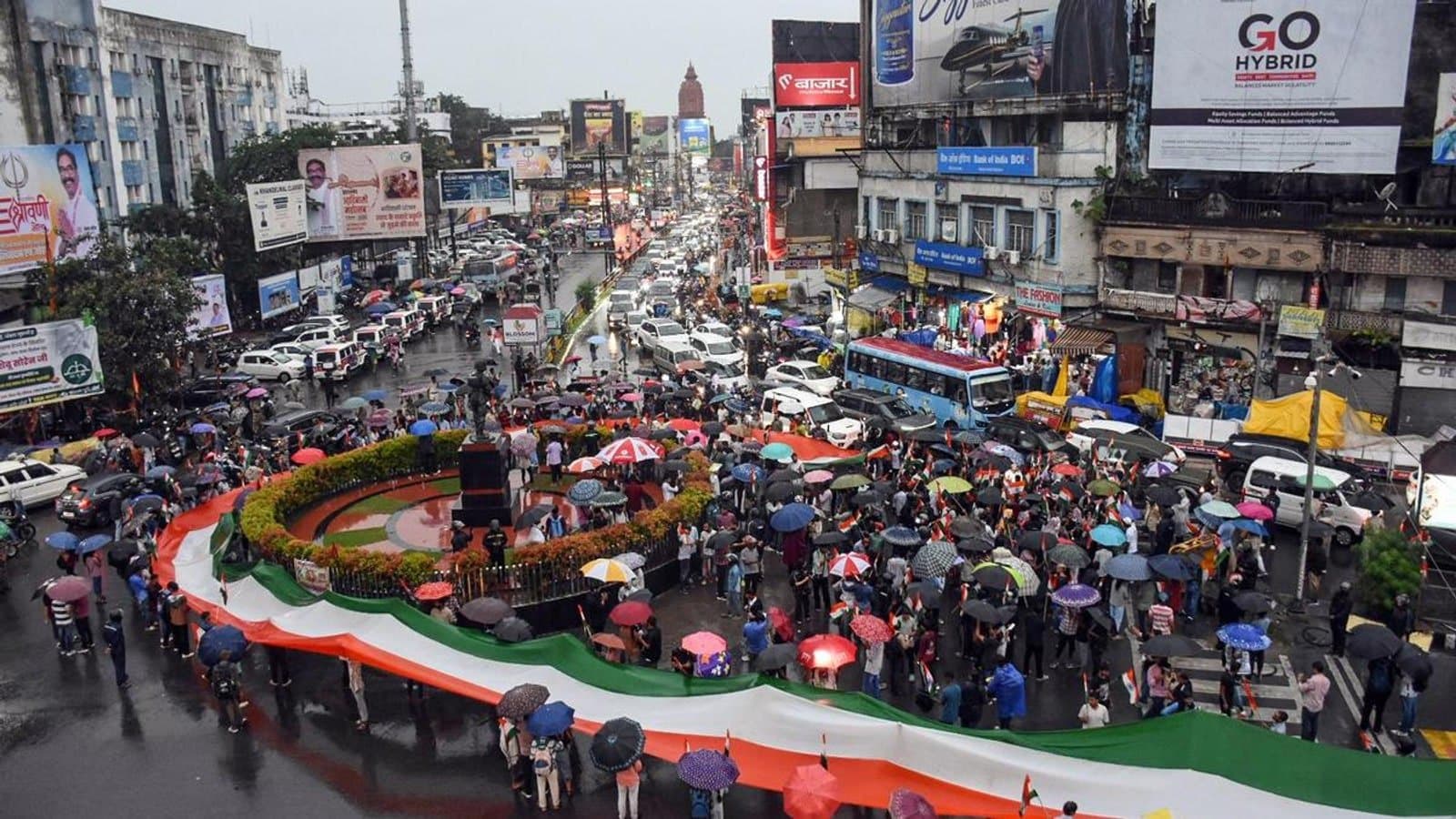 Protesters carrying a long tricolour flag around a traffic circle in the rain in Ranchi, with umbrellas and stalled traffic around them.