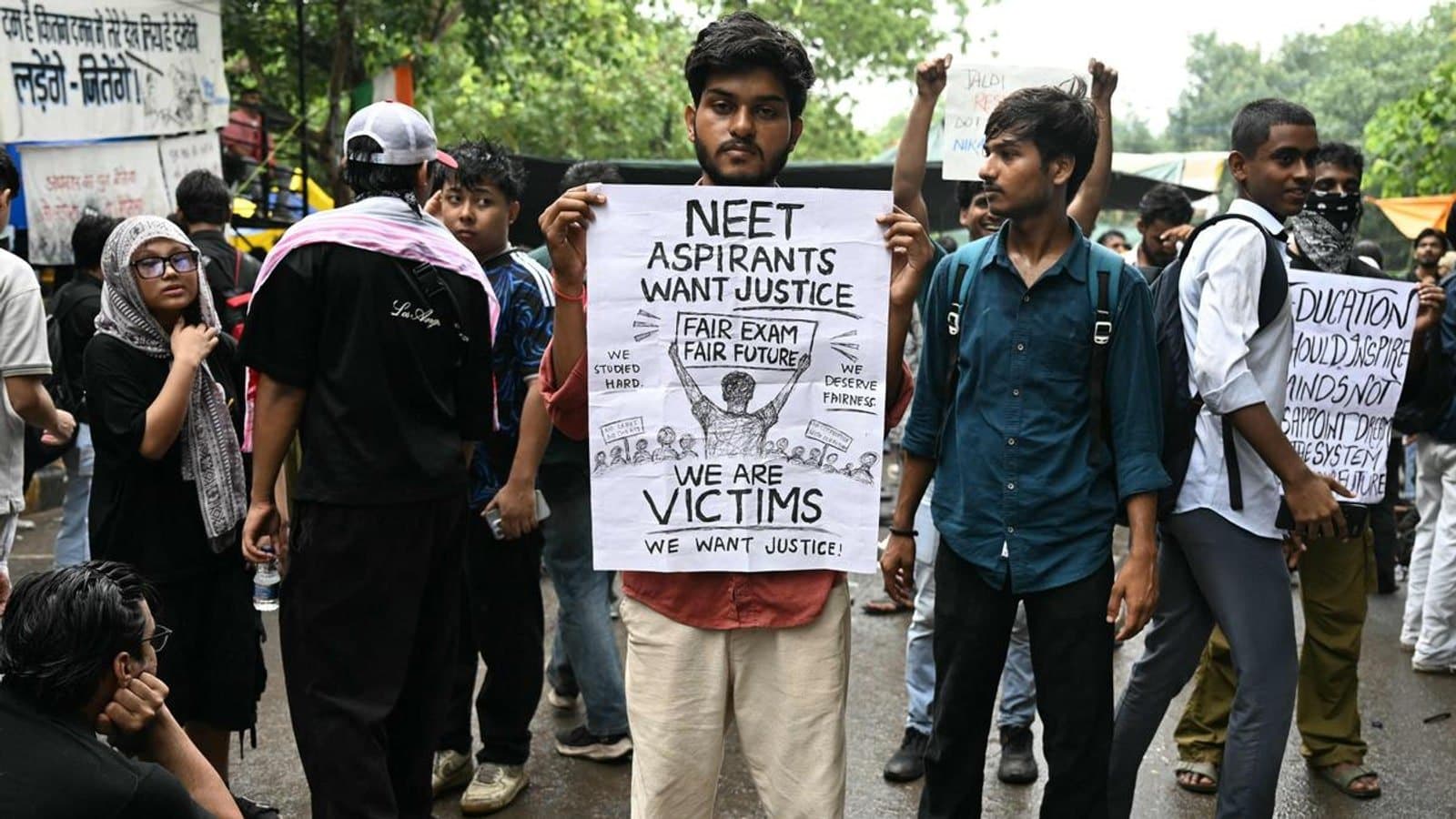 A student at a protest holding a hand lettered placard reading NEET aspirants want justice, fair exam fair future, we are victims. फाइल फोटो।