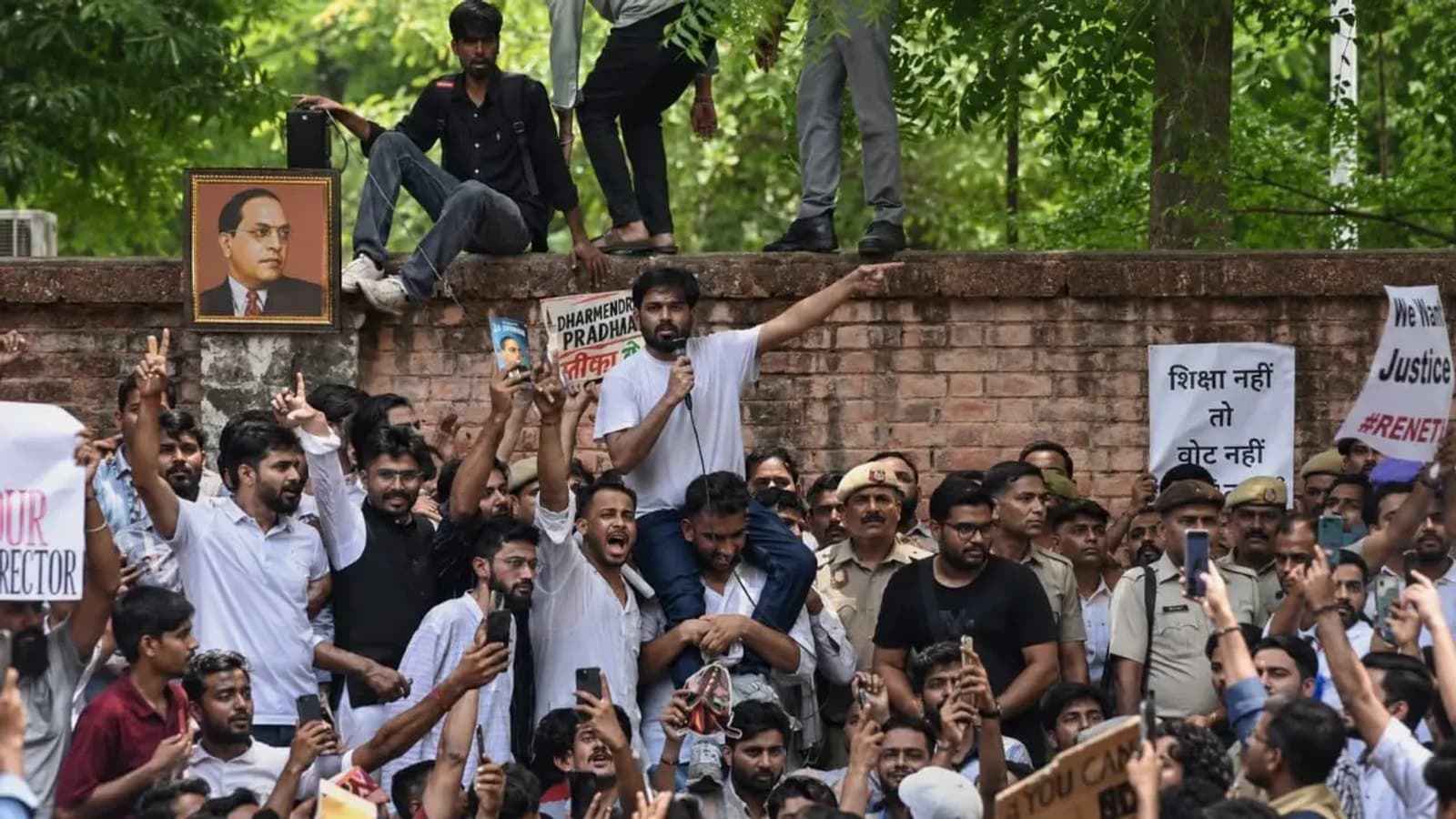 Students at the protest, many filming on phones, with placards in Hindi and English and a portrait of B R Ambedkar on the wall behind. फाइल फोटो।