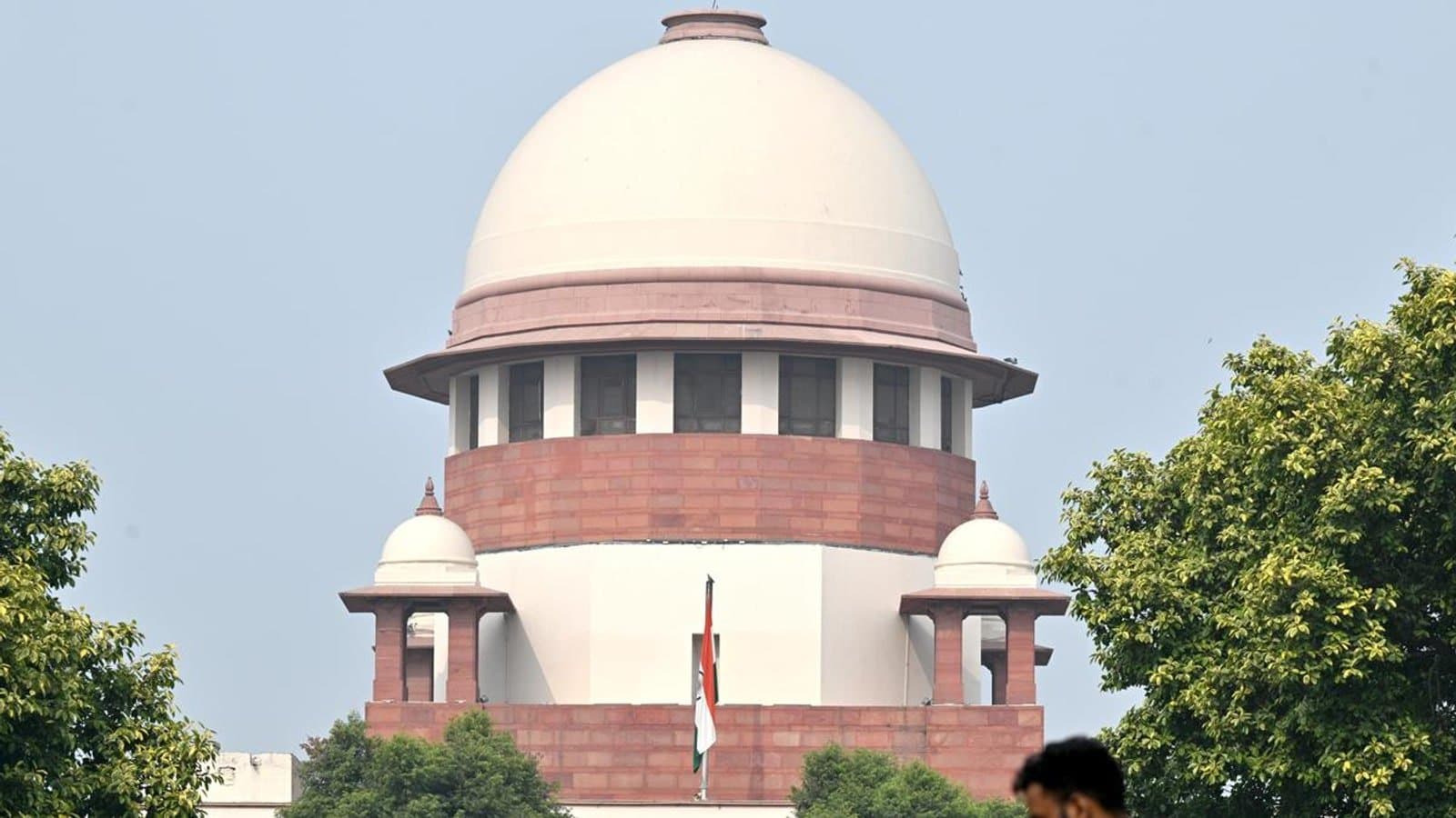 The dome of the Supreme Court building in New Delhi, with the national flag flying below it and trees in the foreground.
