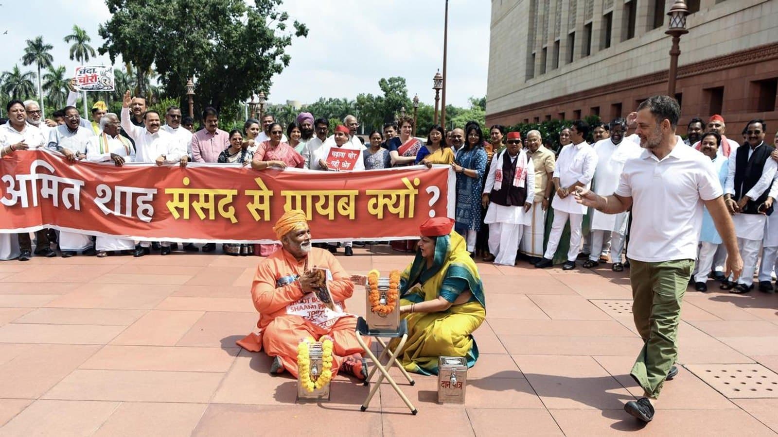 Opposition MPs protesting outside Parliament behind a banner in Hindi, with two of them seated on the ground beside collection boxes during a skit. फाइल फोटो।
