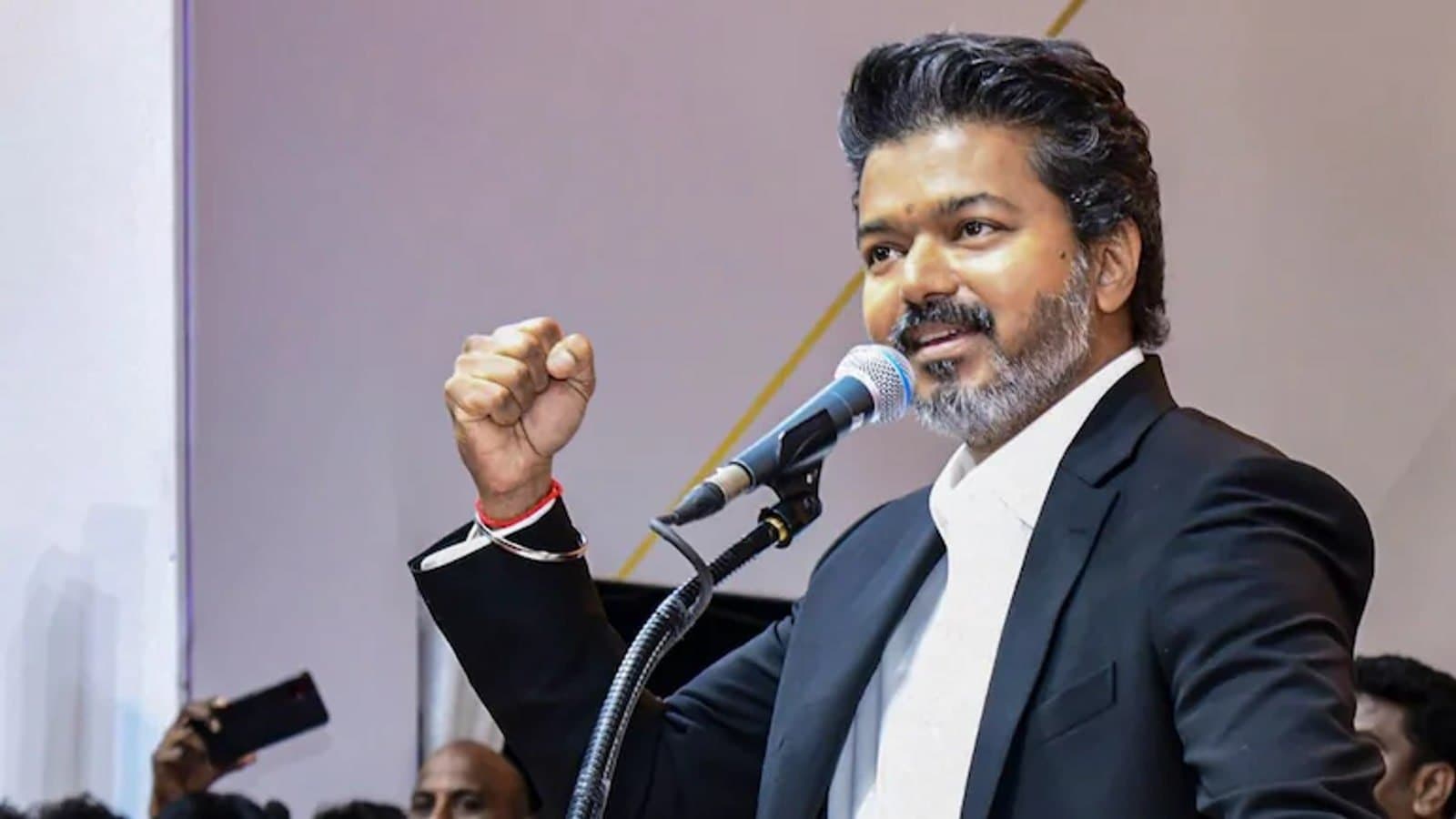 Tamil Nadu Chief Minister Vijay speaking into a microphone with one fist raised at an event. File photograph.