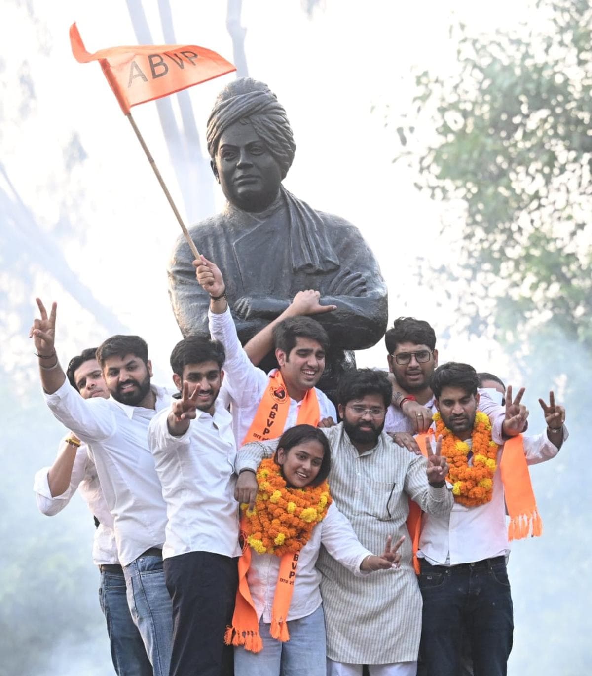 ABVP supporters celebrate with flags and garlands beside a statue of Swami Vivekananda after the DUSU election results