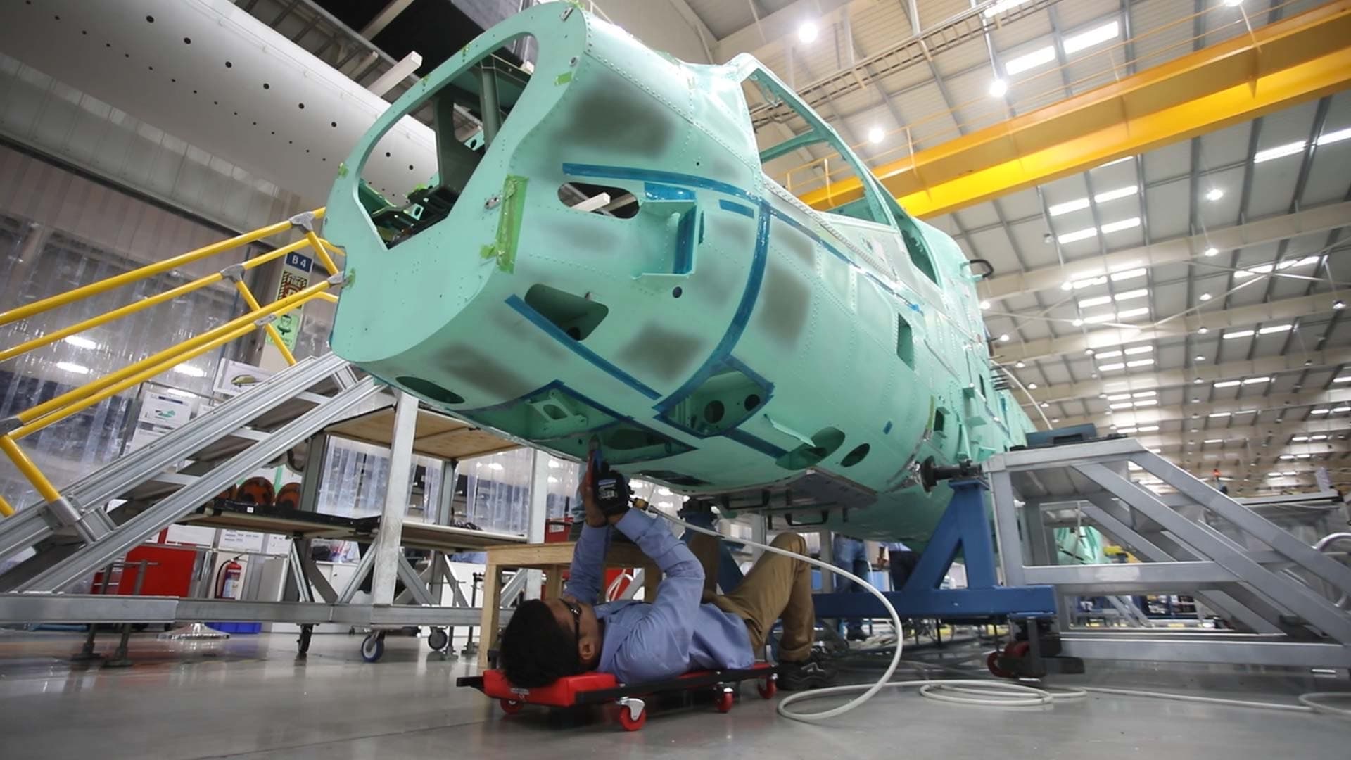 A technician works beneath the fuselage of an aircraft being assembled inside a manufacturing hangar in India