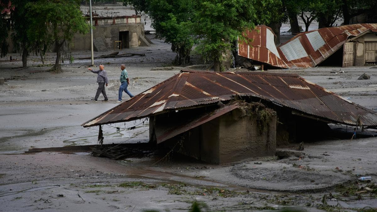 नेपाल में अचानक आई बाढ़ के बाद कीचड़ में दबे ढहे हुए मकान के पास से गुजरते स्थानीय निवासी