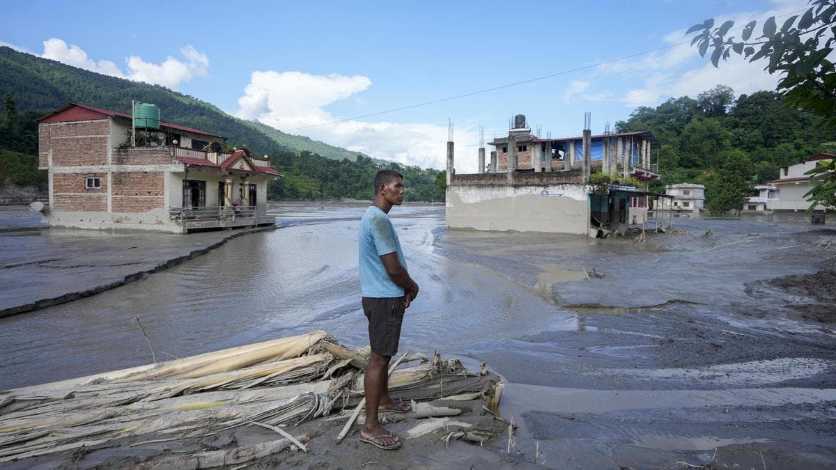 A man stands amid debris looking at flooded and damaged houses in Nepal