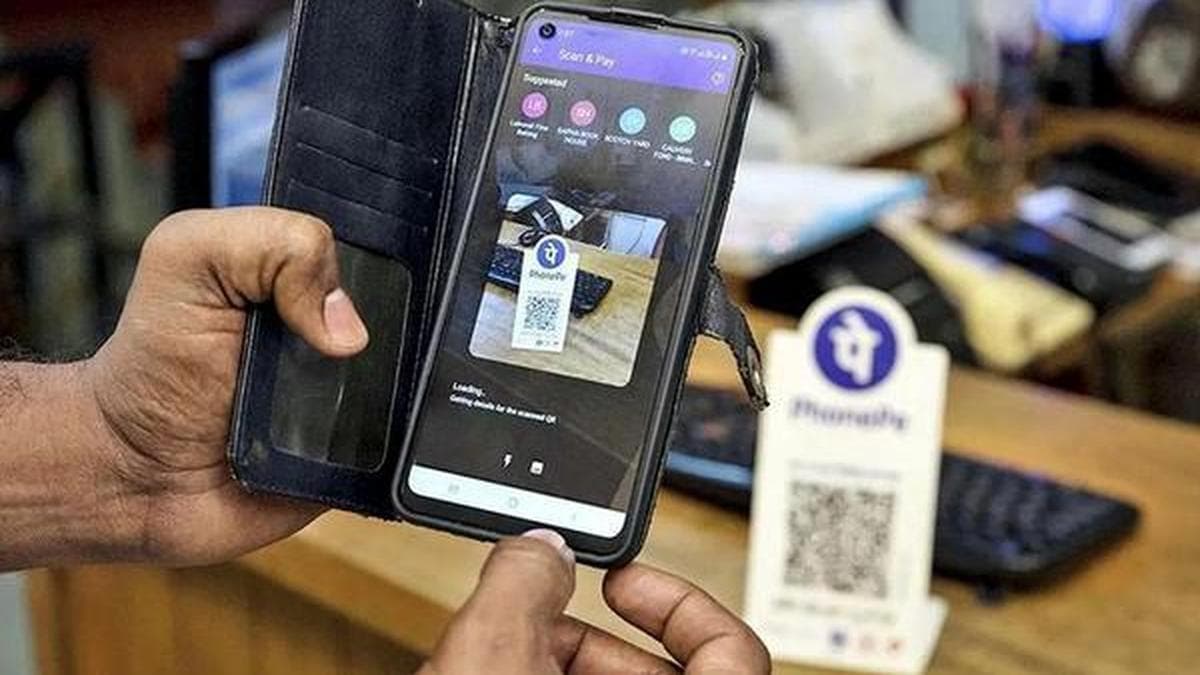 A person scans a UPI QR code on a smartphone to make a payment at a shop counter