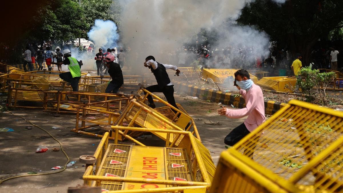 Protesters run through overturned barricades amid tear gas smoke during a demonstration in Delhi