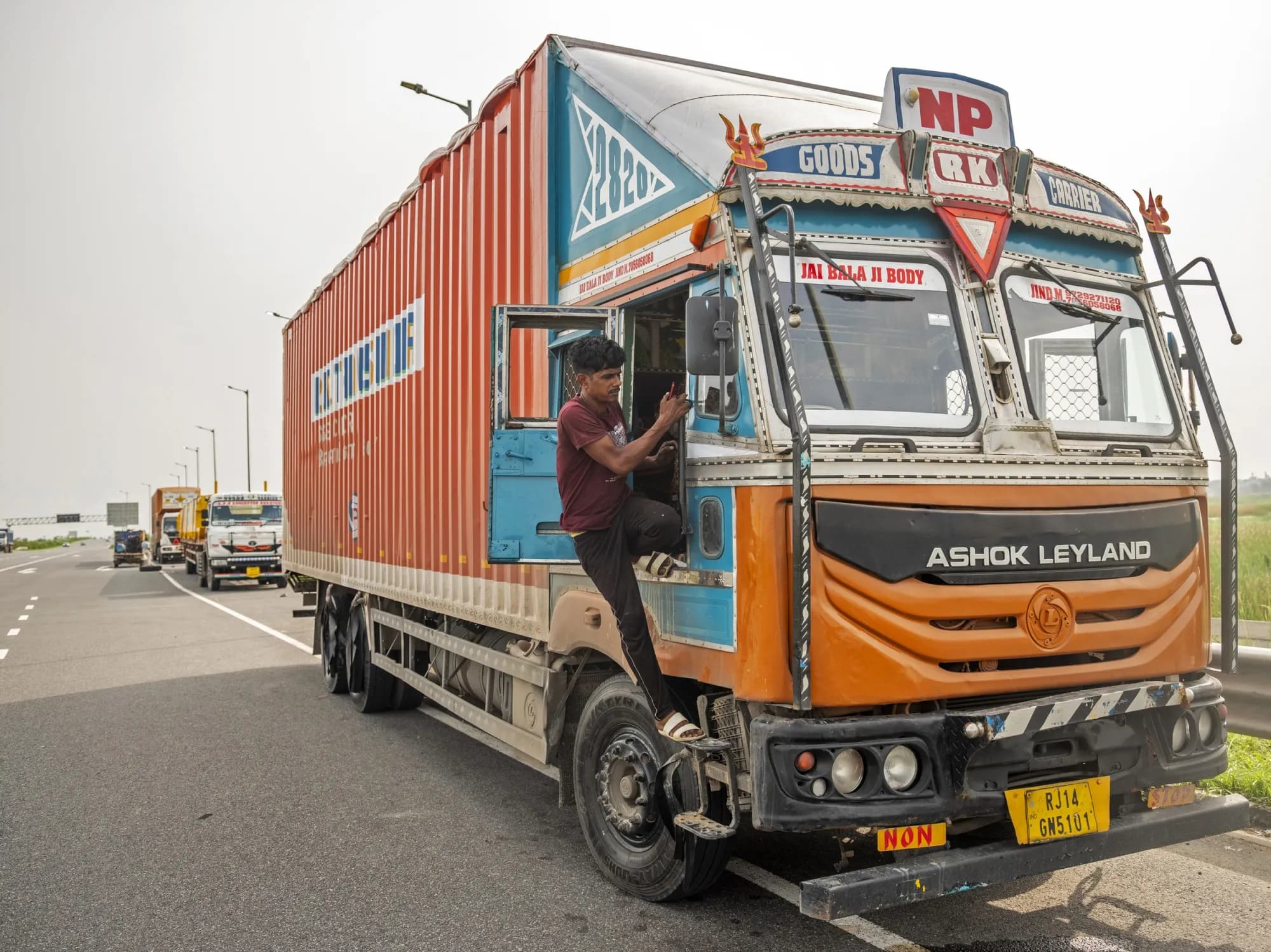 A truck driver climbs into the cab of his Ashok Leyland truck parked on an Indian highway